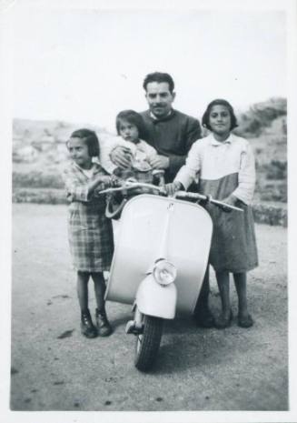 Family crowded around vesper with father on vesper holding an infant an two older girls standing on either side of the vesper holding a handle bar. [Taormina]