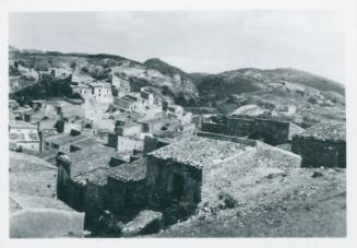Shot of Sicilian town. Hills and scrubland in background. Hill that the the picture was taken from slightly visible in the bottom frame.