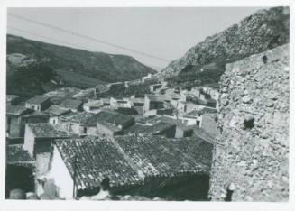 Village nestled in a valley between two mountain ridges. A wall of a building is in the right foreground