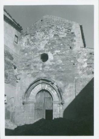 The entrance to a building, probably a church. The door is arched and has a heraldic sign on it and above this there is a circular window