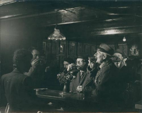 Wilhelmina Barns-Graham and men drinking in the Sloop, St Ives. Information on reverse.  [Central Office of Information]