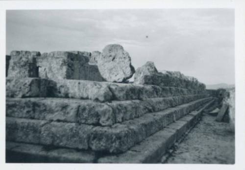 Ground shot of the steps leading up to what once was a temple and is now an exposed flat plain with the bases of fallen columns scattered around. Shot from the right