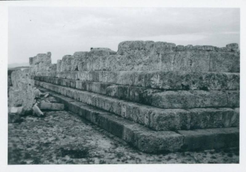 Ground shot of the steps leading up to what once was a temple and is now an exposed flat plain with the bases of fallen columns scattered around. Shot from the left