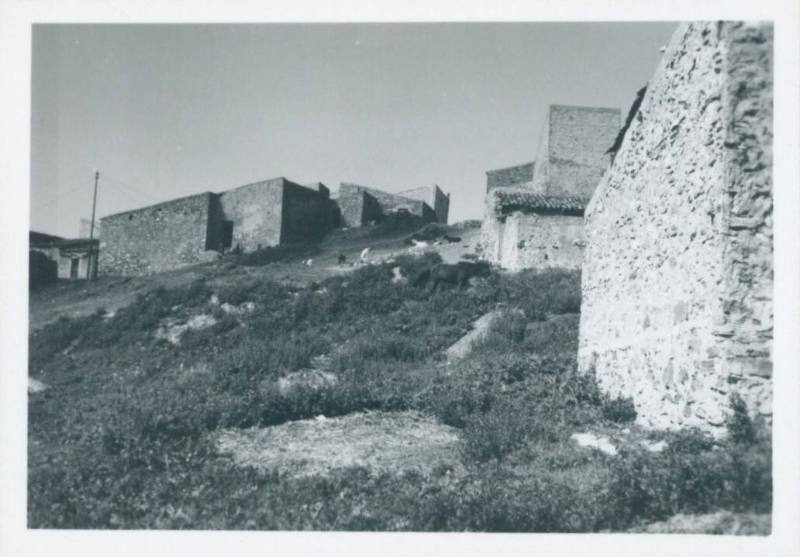 Small stone buildings in a town in the Italian countryside with a stone wall in the righthand side of the frame [Palinuro]