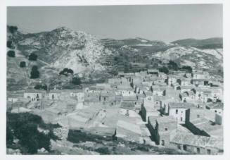 Sicilian town with snowy mountains in background. Scrubland in bottom of frame.