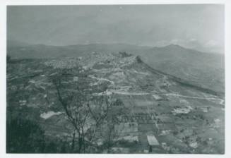 Sicilian hilly countryside. In the center of the frame a hill rises with a town on its top. Castle/church/other prominent building is visible