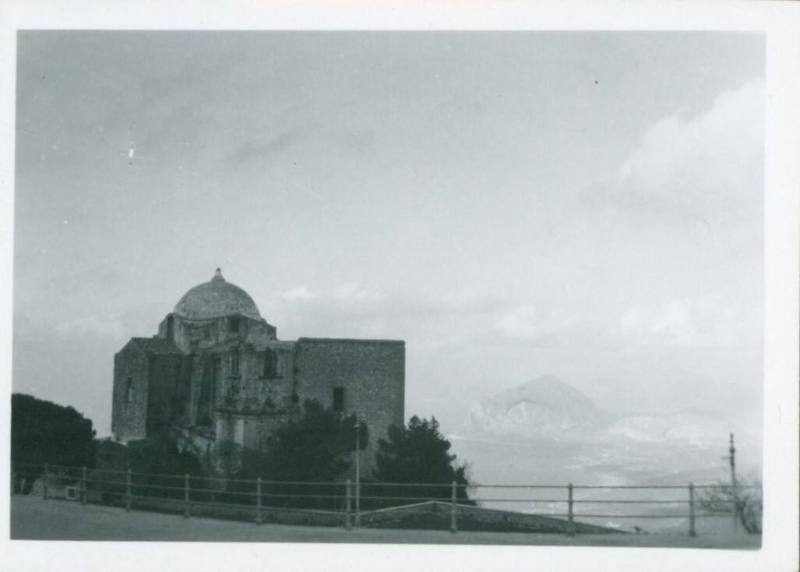 A church with a small dome fills the left of the frame while the ocean in is the background and to the right in the far distance a hillly pennisula can be seen