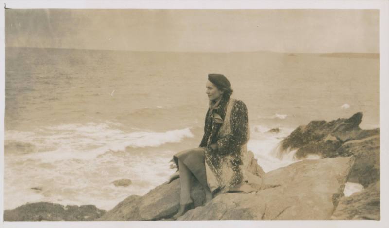 Wilhelmina Barns-Graham sitting on rock in fur coat and beret, looking out to sea. [Clodgy]